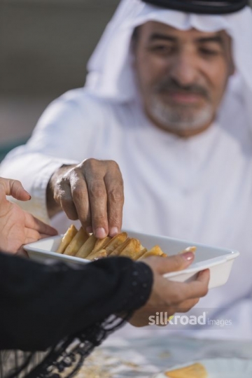 Arab man filling up his plate by taking food from the woman|-