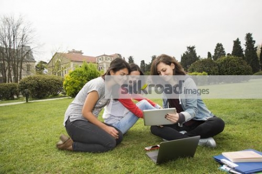 Women sitting together on the grass working|