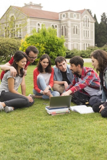 Students on the grass looking at something on the laptop 