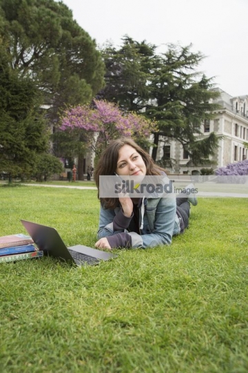 University Student laying down on the grass talking on the phone|