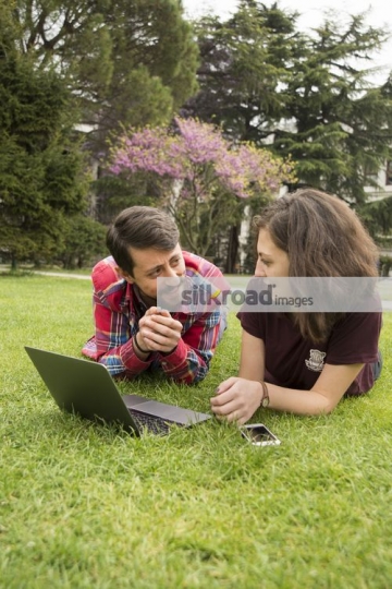 Students laying down on the grass talking|