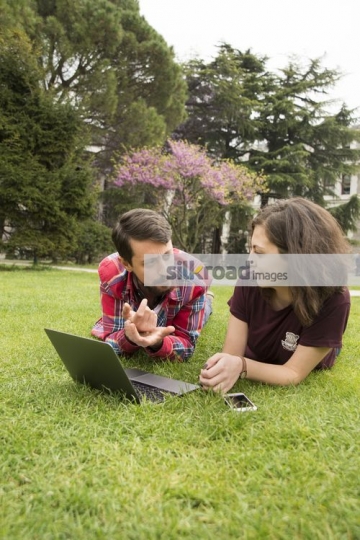 University Student laying down on the grass talking|