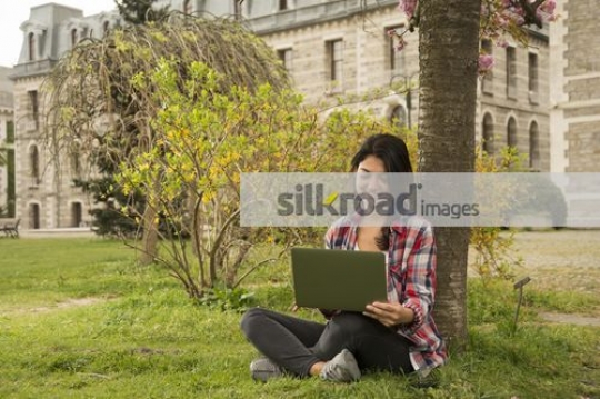 European woman sitting on the grass using the laptop|