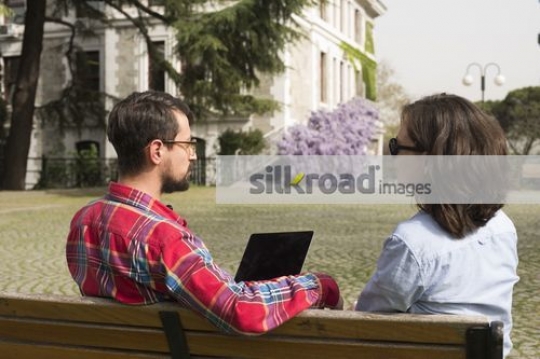 Man sitting on the bench with woman using the laptop |