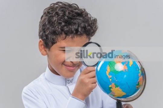 Middle Eastern kid looking at the globe with a magnifying glass 