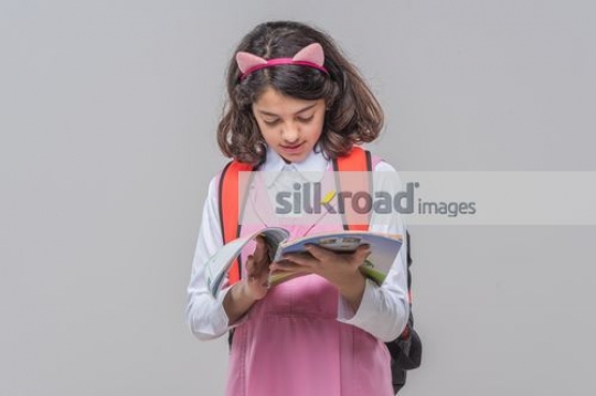 Arab girl carrying her school bag reading the book|