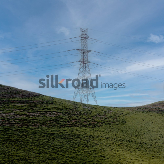 Power Line and Electricity Tower on Rolling Hills Under Blue Sky