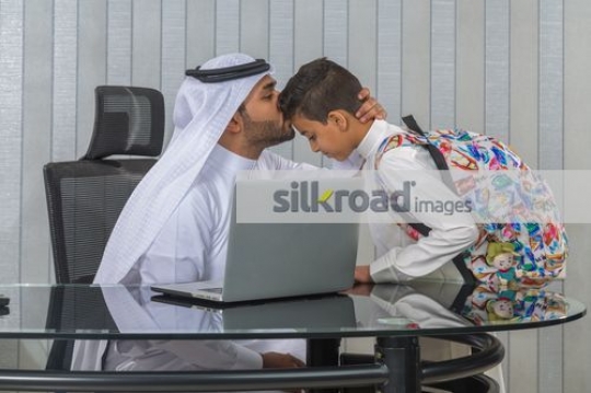 Middle Eastern father kissing young boys forehead|
